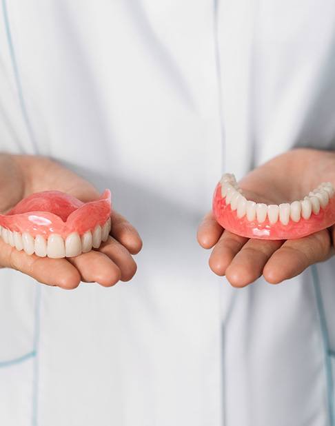 Hands at abdomen level each holding an arch of dentures