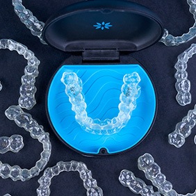 Bird’s eye view of several Invisalign trays on black surface surrounding carrier case