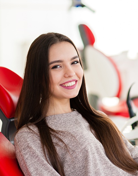 Woman in red dental chair with long hair smiling
