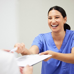 a front desk staff member handing forms to a patient