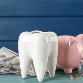 A large ceramic tooth sitting next to a piggy bank and dollar bills