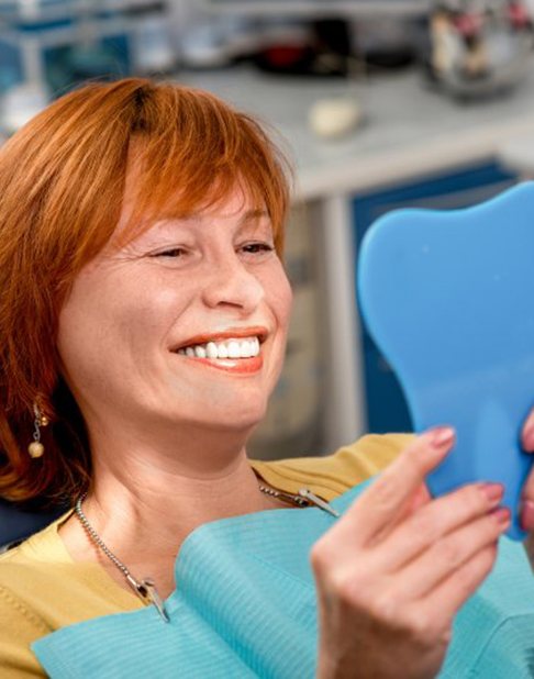 Patient smiling in mirror while sitting in the patient’s chair