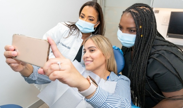 Young woman in dental chair taking selfie with her New York City dentist and dental team member