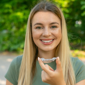 Woman in green shirt holding Invisalign aligner outside