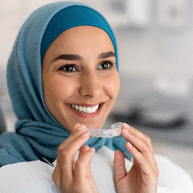 Woman sitting in dental chair smiling and holding clear aligner