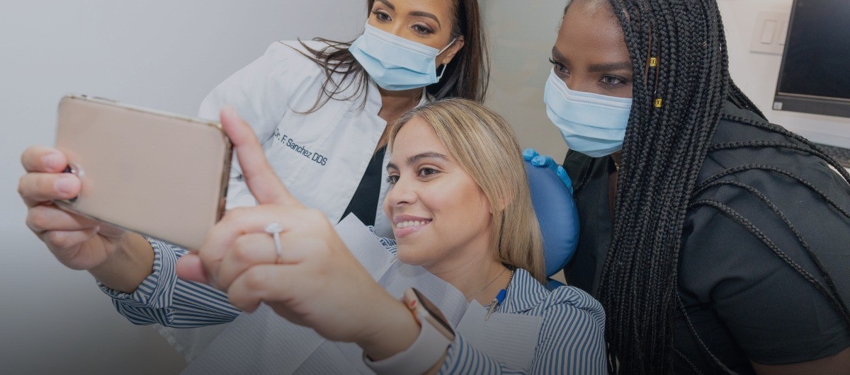 Dental patient taking picture with dentist and team member after cosmetic dentistry treatment