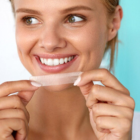 woman smiling while holding teeth whitening strip