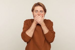 man covering mouth looking embarrassed 