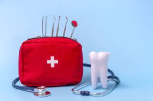 Model tooth next to a red emergency kit full of dental instruments on a blue background