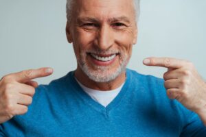 Man with dentures smiling and pointing to his teeth